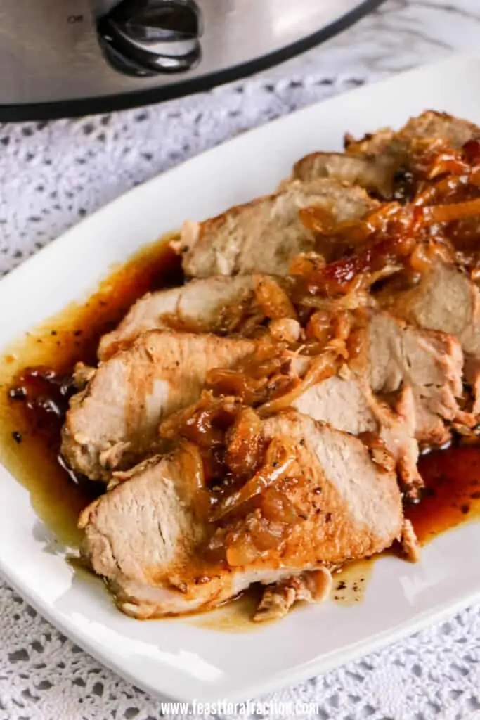 slices of slow cooked pork loin roast on white plate with onions and sauce