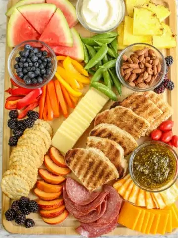 overhead view of charcuterie board with summer fruits and vegetables, bread and cheese