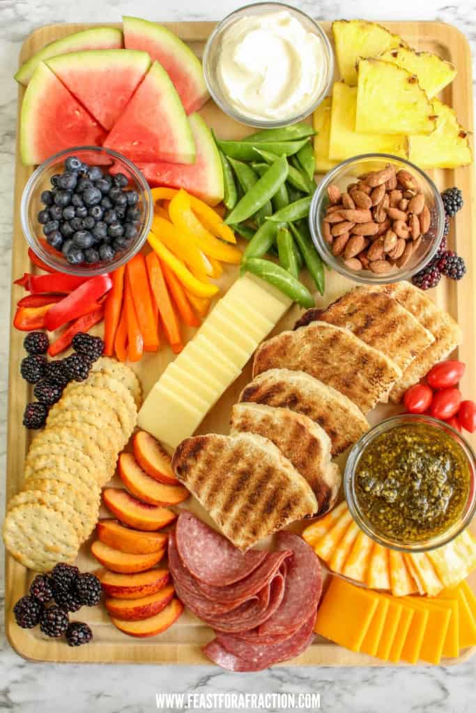 overhead view of charcuterie board with summer fruits and vegetables, bread and cheese