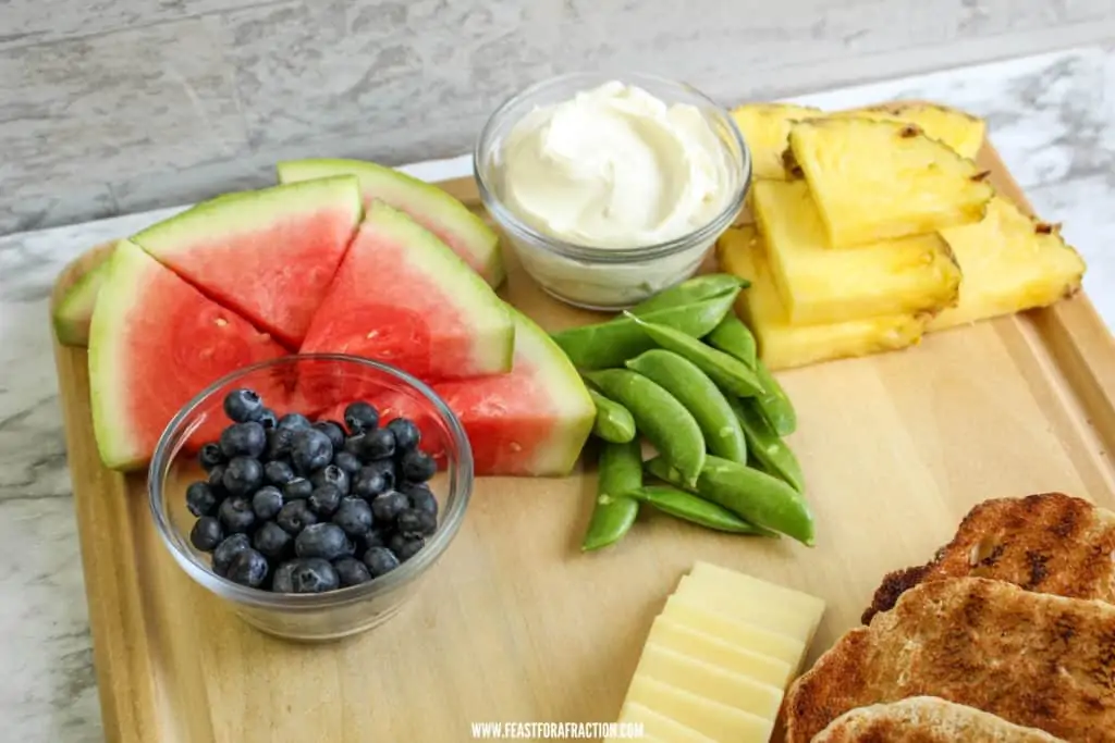 watermelon, pineapple, peas, blueberries, cheese and bread on cutting board