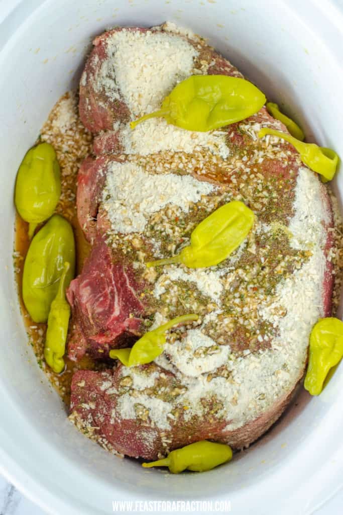 uncooked beef roast in crockpot with ranch seasoning, pepperoncini peppers, and onion soup mix