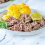 shredded mississippi pot roast on white plate with corn casserole