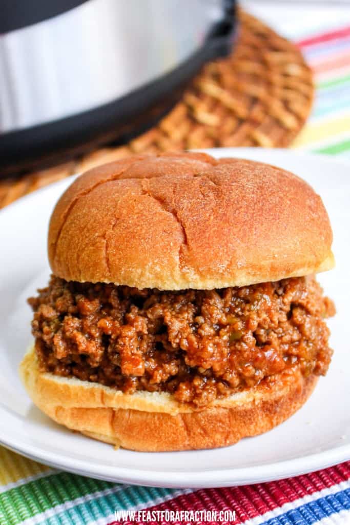 vertical image of sloppy joe sandwich on white plate with instant pot in background