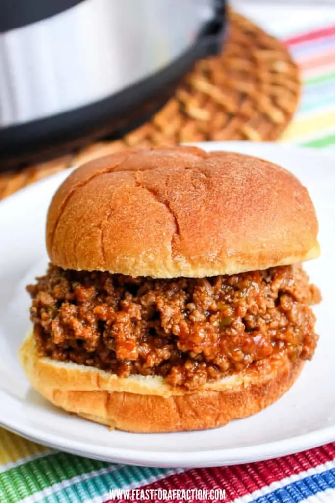 vertical image of sloppy joe sandwich on white plate with instant pot in background