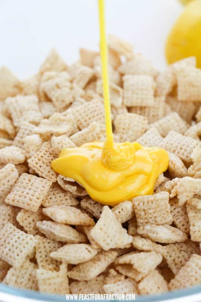 yellow candy melts being poured over chex cereal in glass bowl