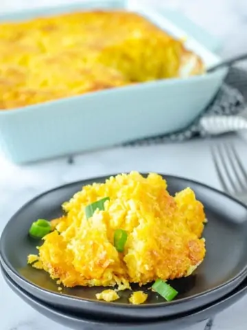 corn casserole garnished with green onions on black plate