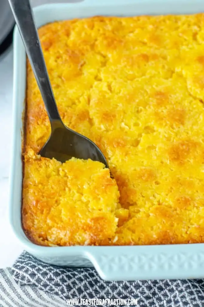 baked corn casserole in blue casserole dish with spoon