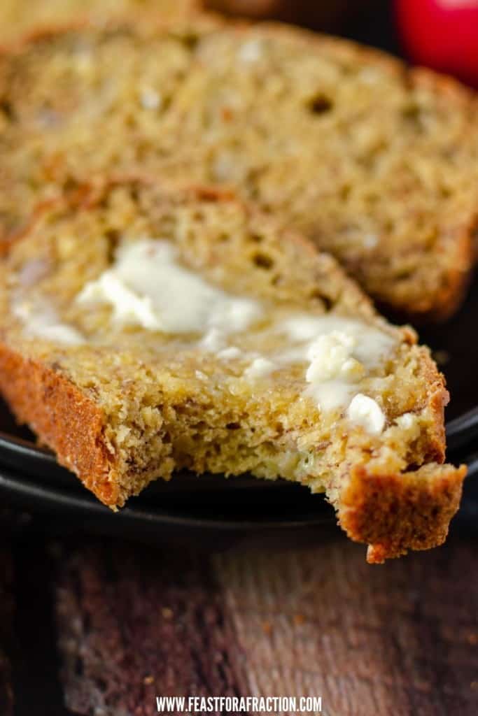 slice of applesauce banana bread on black plate with melted butter and bite taken out