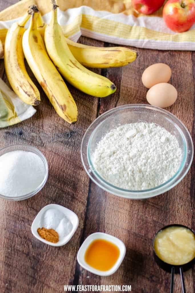 bananas, eggs, flour, sugar, salt, baking soda, cinnamon, vanilla and applesauce in bowls on counter