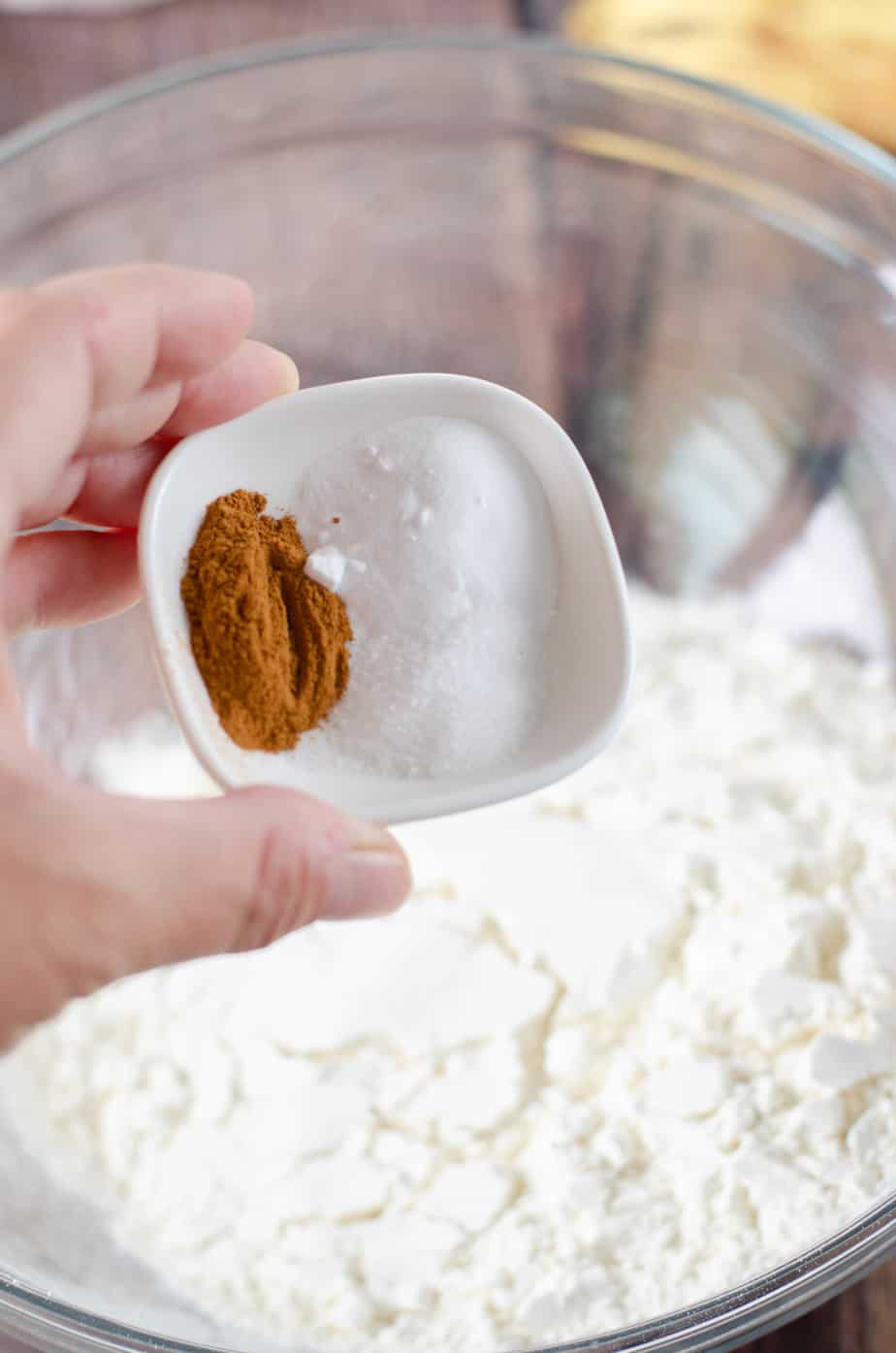 cinnamon, salt and baking soda being added to a bowl of flour