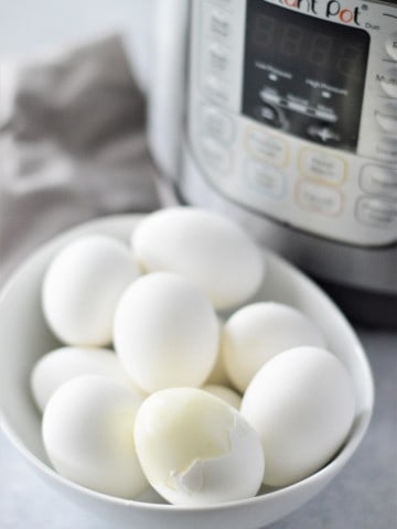 peeled hard boiled egg in a bowl with unpeeled hard boiled eggs and instant pot in background