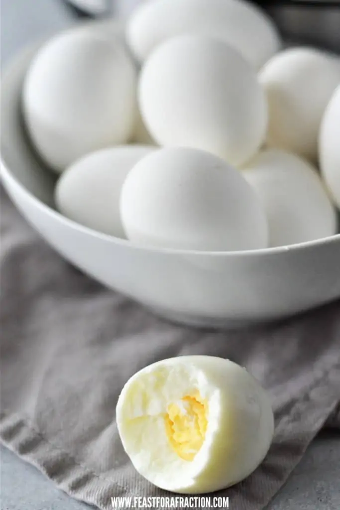 hard boiled egg with bite taken out and bowl of instant pot hard boiled eggs