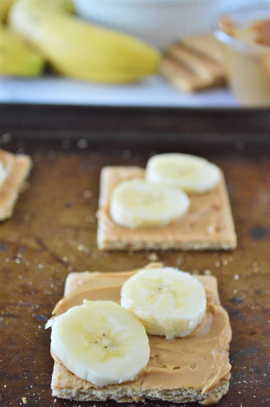 graham crackers spread with peanut butter and topped with sliced bananas on cookie sheet