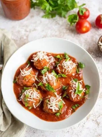 oven baked meatballs in white bowl with tomato sauce and shredded parmesan cheese