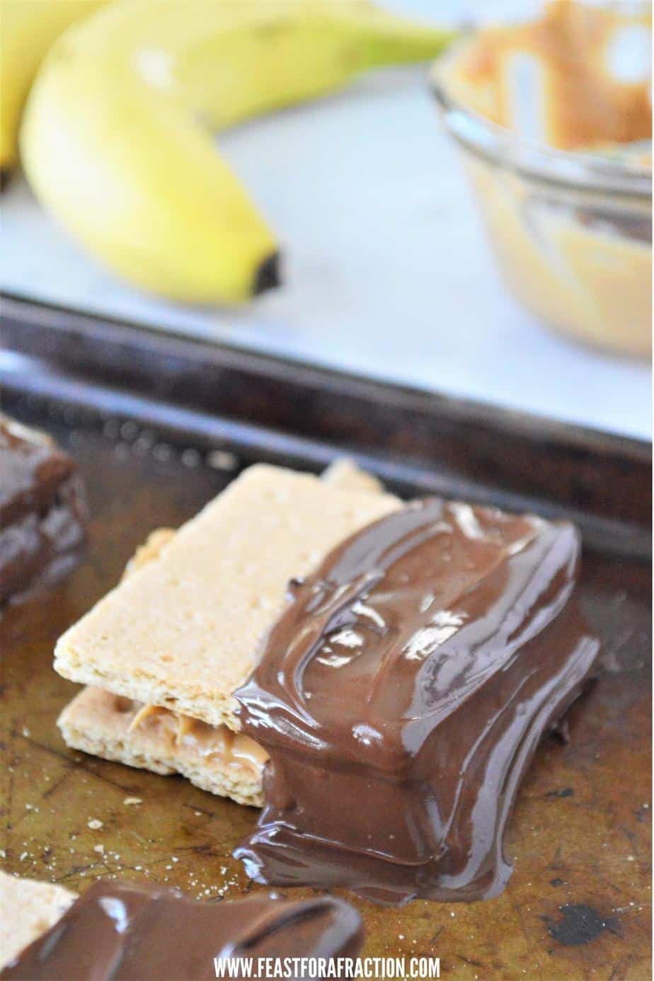 graham crackers with peanut butter and banana dipped in chocolate cooling on cookie sheet