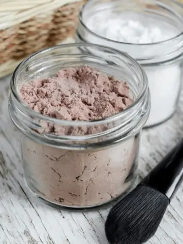 jars of dry shampoo on counter with make-up brush