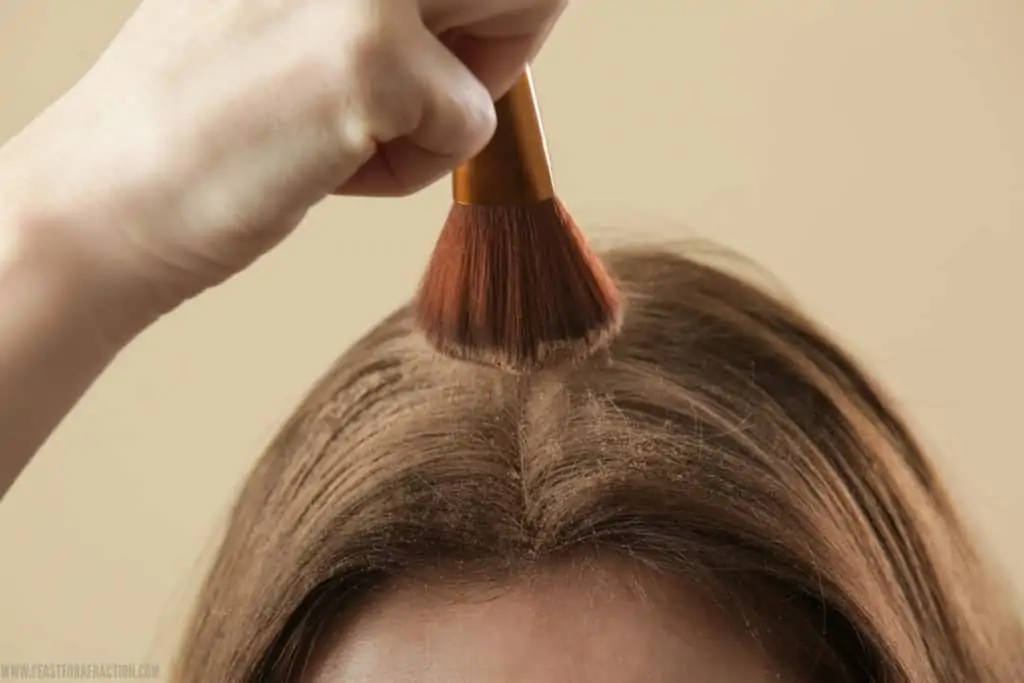 girl applying dry shampoo with make-up brush to hair
