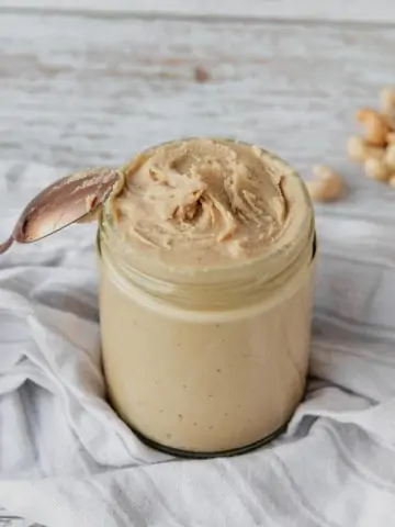 jar of homemade cashew butter with spoon leaning against jar and roasted cashews on counter