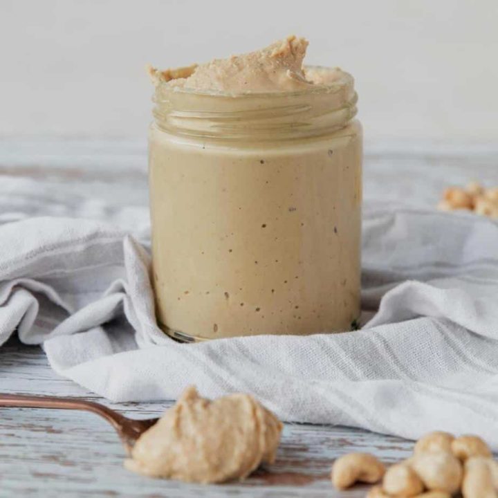 homemade cashew butter in jar with cloth napkin and spoon of nut butter