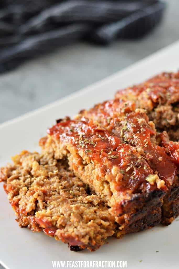 side angle of stuffing meatloaf sliced on white plate garnished with italian seasoning and ketchup glaze