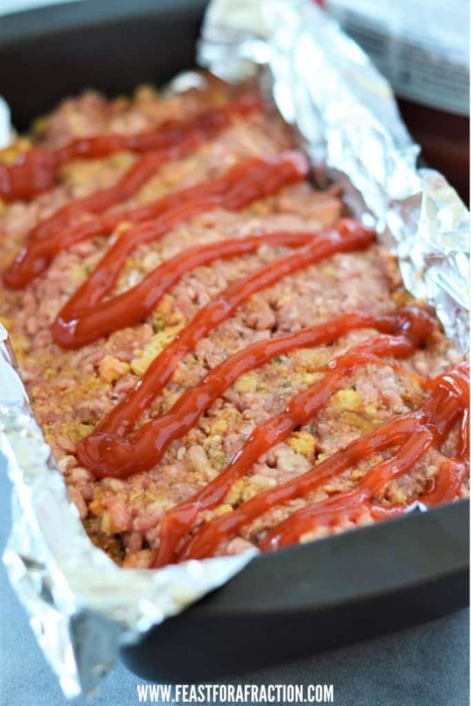 stuffing meatloaf mixture in foil-lined loaf pan topped with ketchup