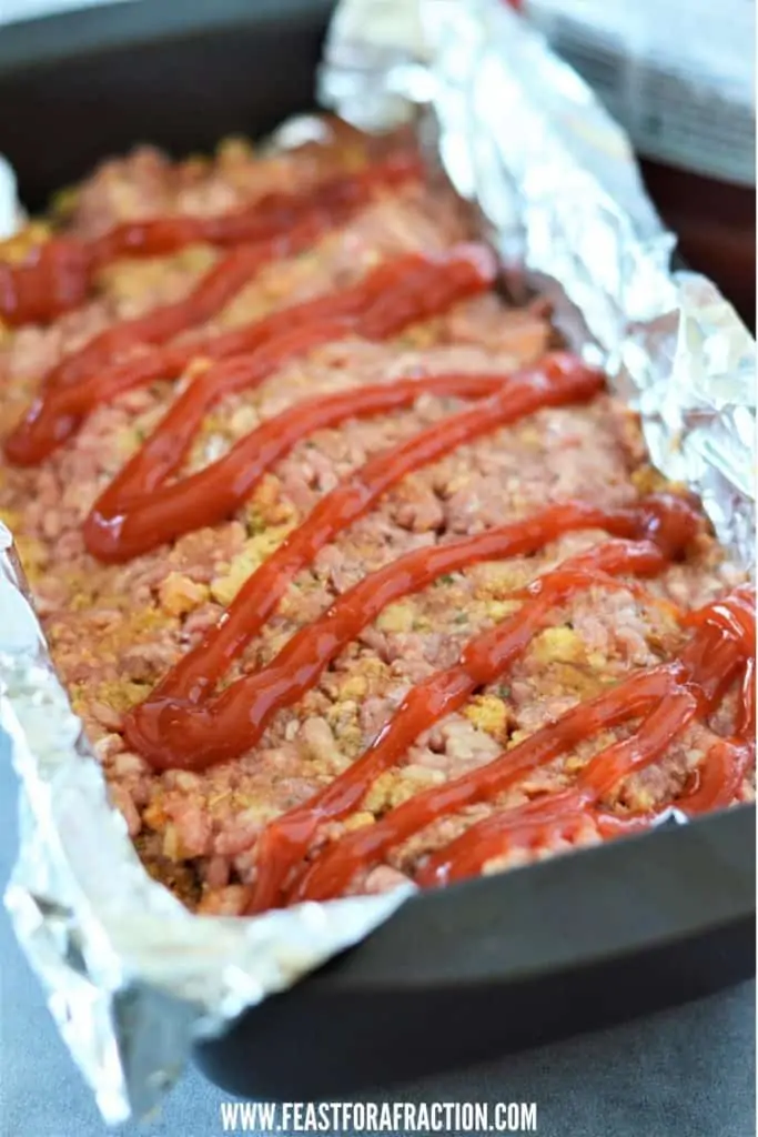 stuffing meatloaf mixture in foil-lined loaf pan topped with ketchup
