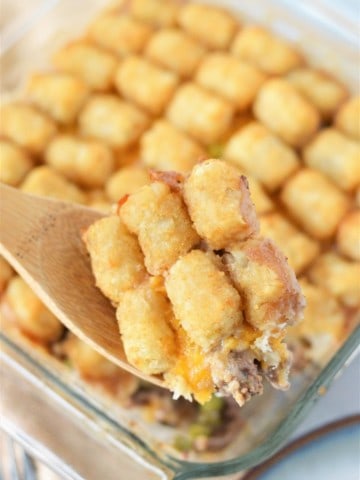 baked tater tot casserole on counter with wooden spoon taking out a scoop