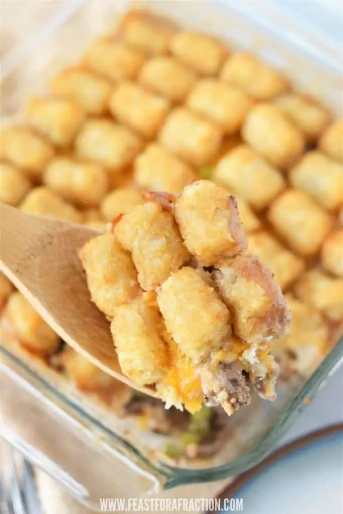 baked tater tot casserole on counter with wooden spoon taking out a scoop