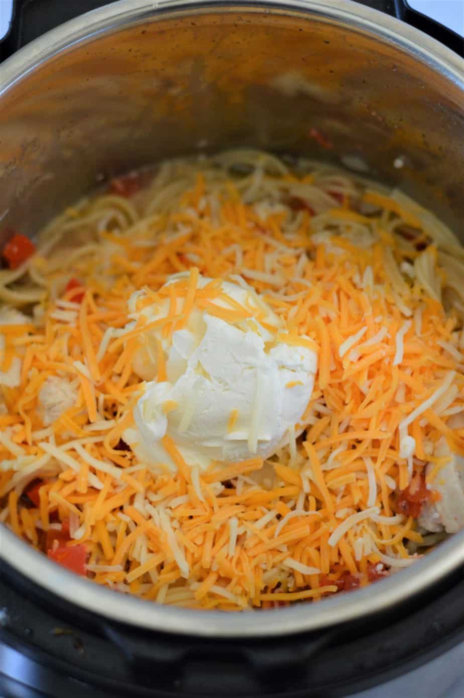 cream cheese and shredded cheese added to instant pot containing spaghetti, chicken and rotel