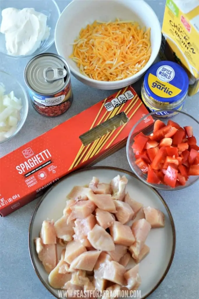 ingredients for chicken spaghetti: cubed chicken breast, spaghetti, chopped onion, chopped red pepper, garlic, can of Rotel, cream cheese, shredded cheese and chicken stock