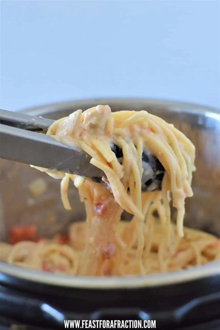 tongs holding instant pot chicken spaghetti above instant pot