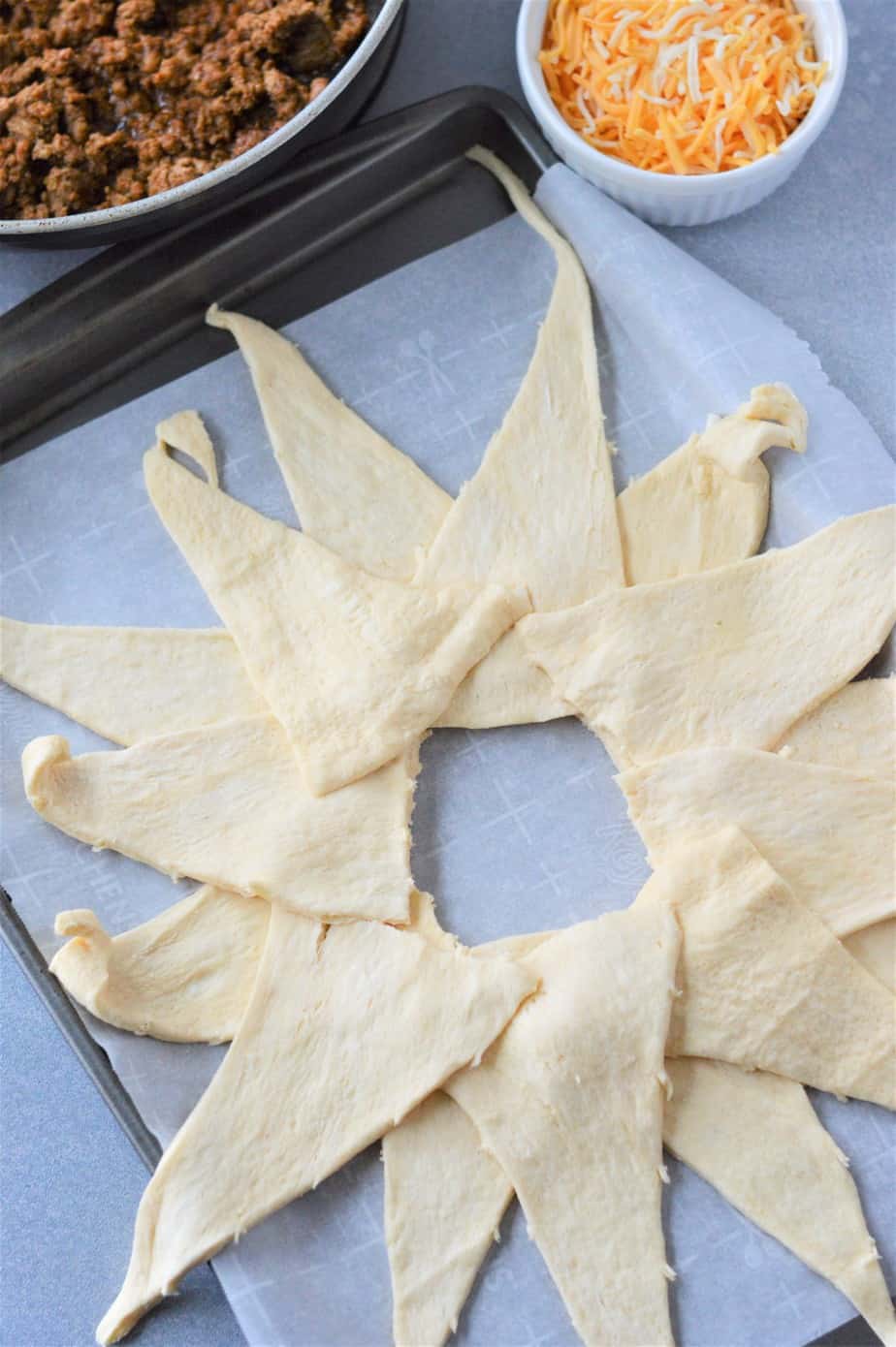 crescent roll dough layered to form a circle with ground beef and shredded cheese in bowls to the side