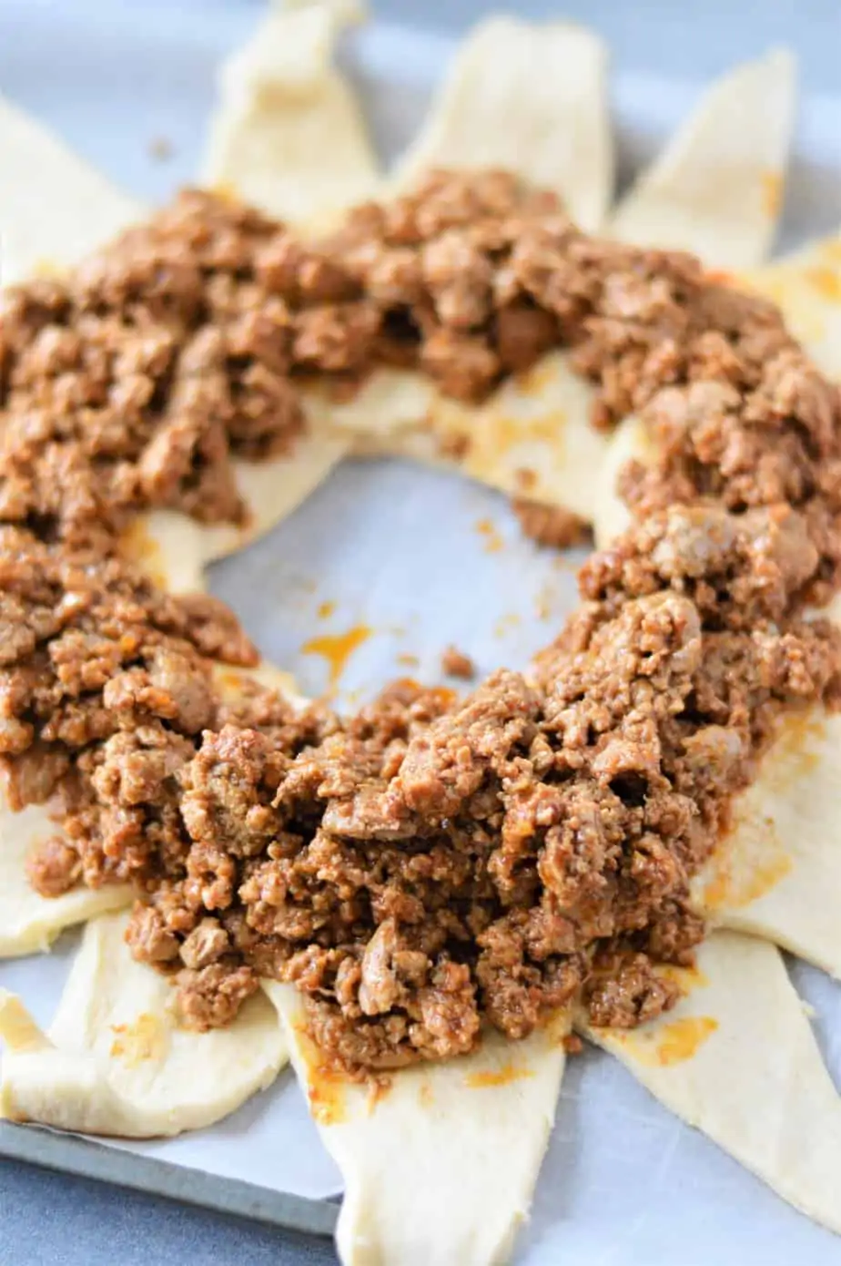 cooked seasoned ground beef layered on top of crescent roll dough in the shape of a ring