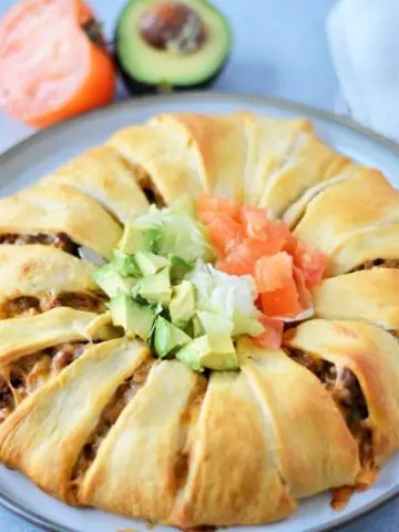 baked crescent roll taco bake on gray platter with avocado and tomato in background