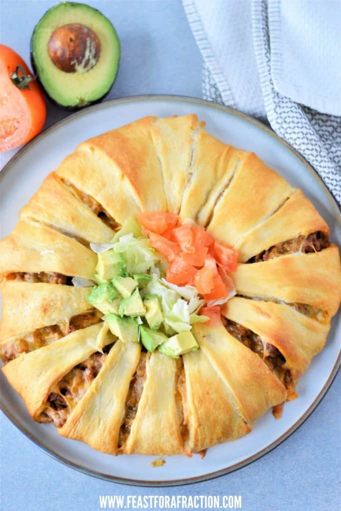 overhead view of baked crescent roll taco ring with avocado half and cut tomato to side