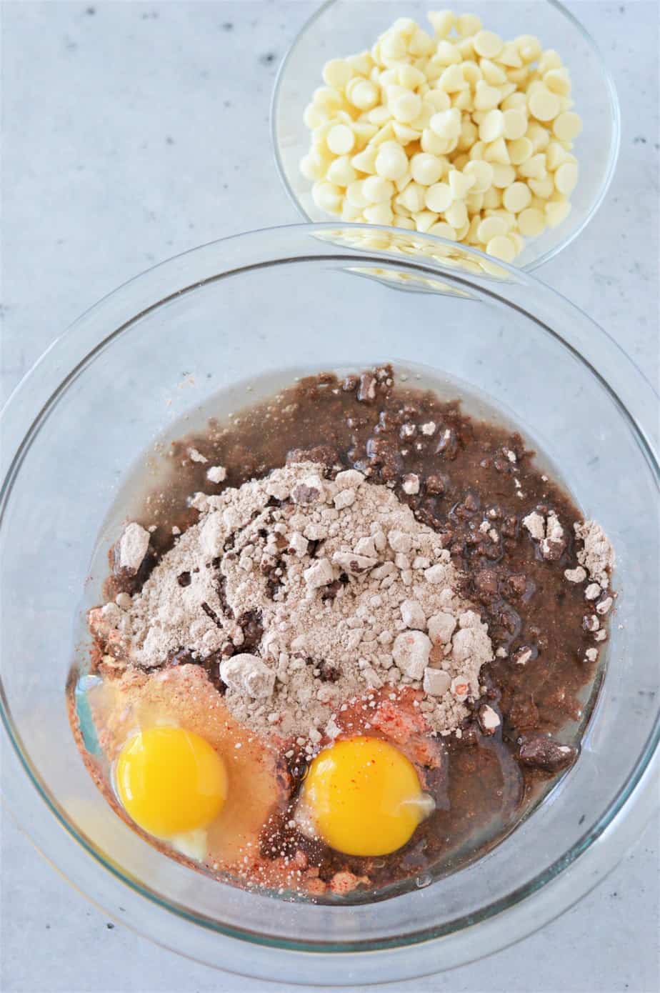 red velvet cake mix, oil, and eggs in glass bowl with small bowl of white chocolate chips to the side