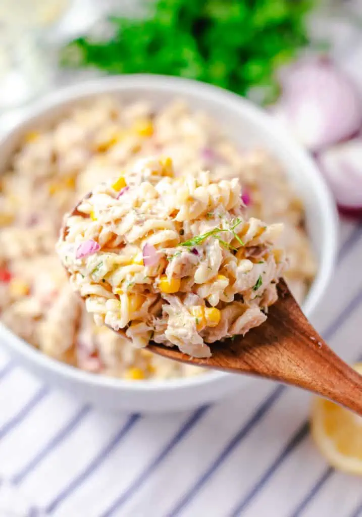 wooden spoon scooping tuna pasta salad from white bowl