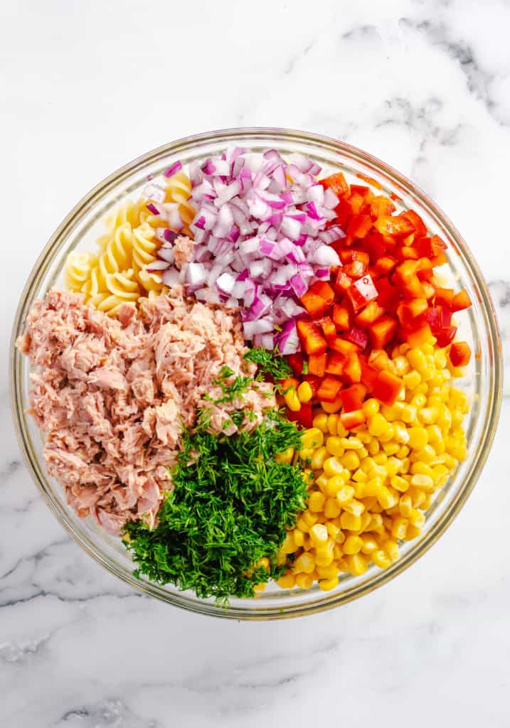 tuna, pasta, red onion, red bell peppers, corn and parsley in glass bowl