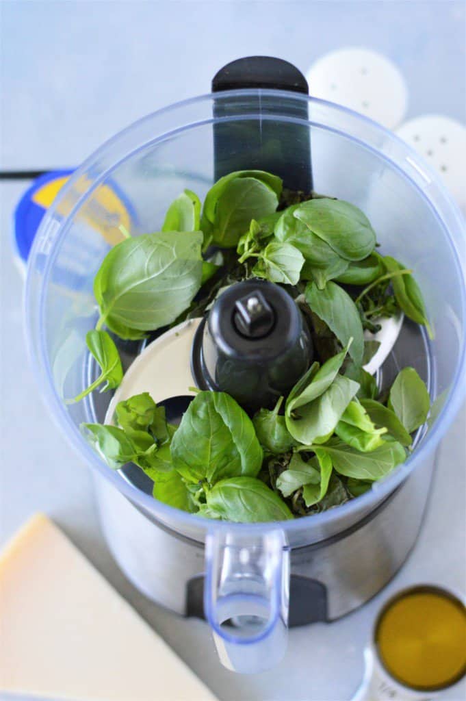 ingredients for homemade pesto on counter and basil leaves in food processor