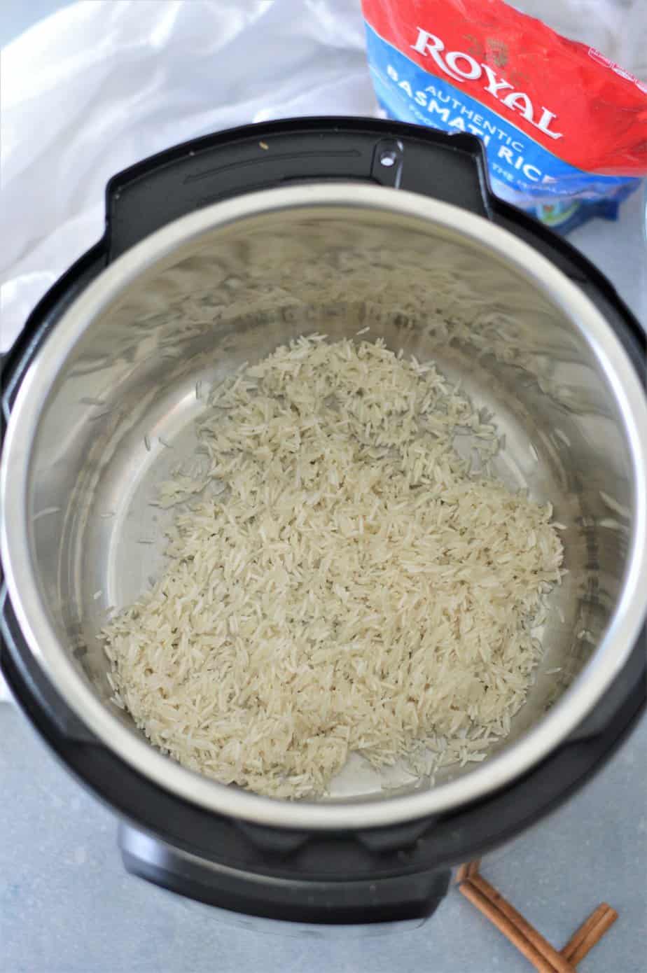 rinsed Basmati rice in instant pot with towel and cinnamon stick in background