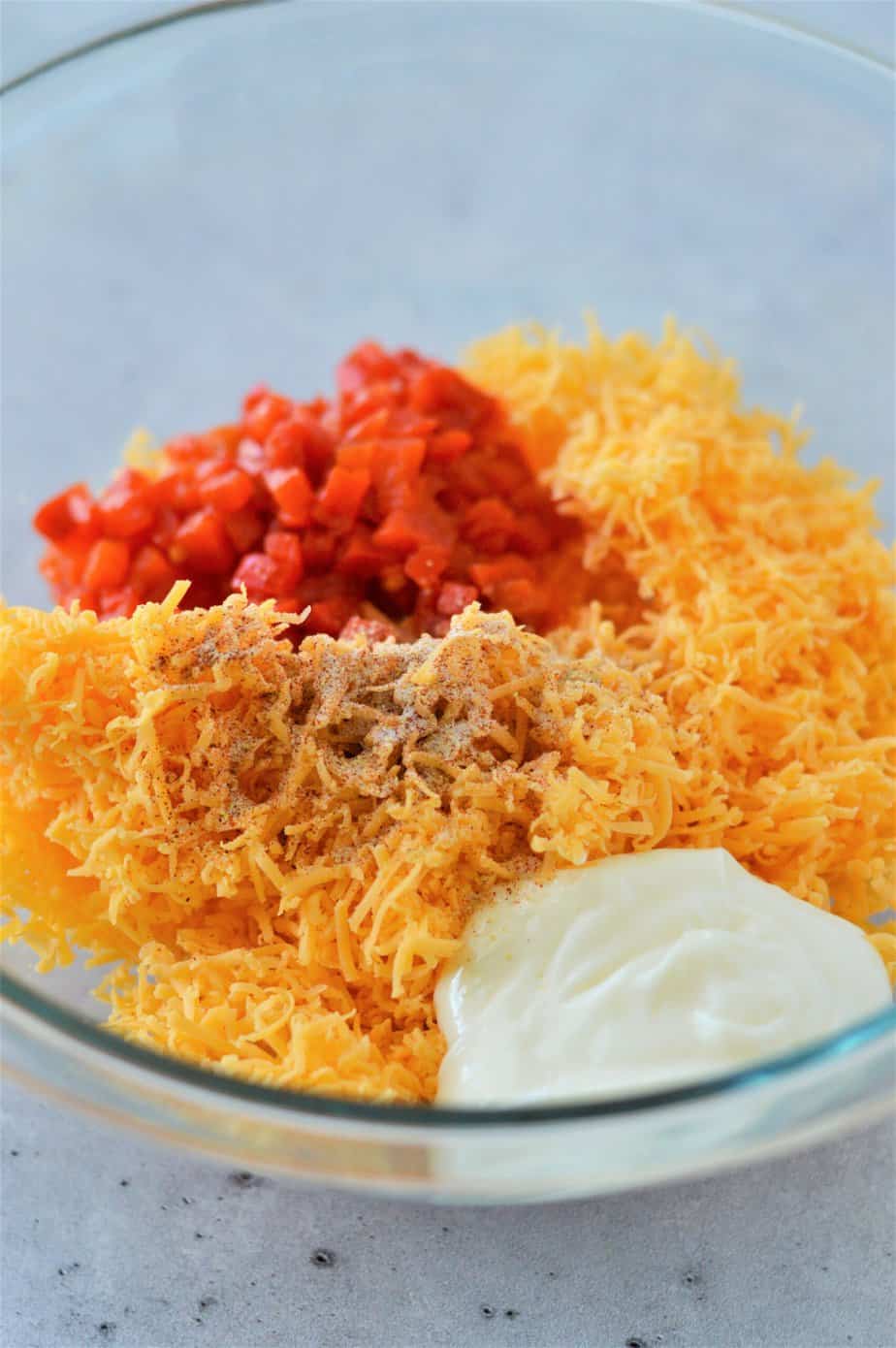 shredded cheese, mayonnaise, diced pimentos and spices in glass bowl