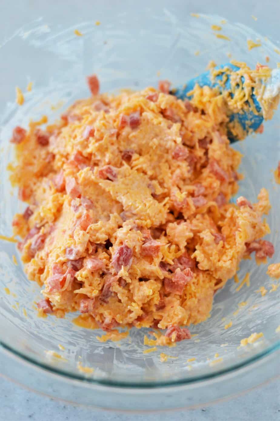 pimento cheese mixed in a glass bowl with blue spatula