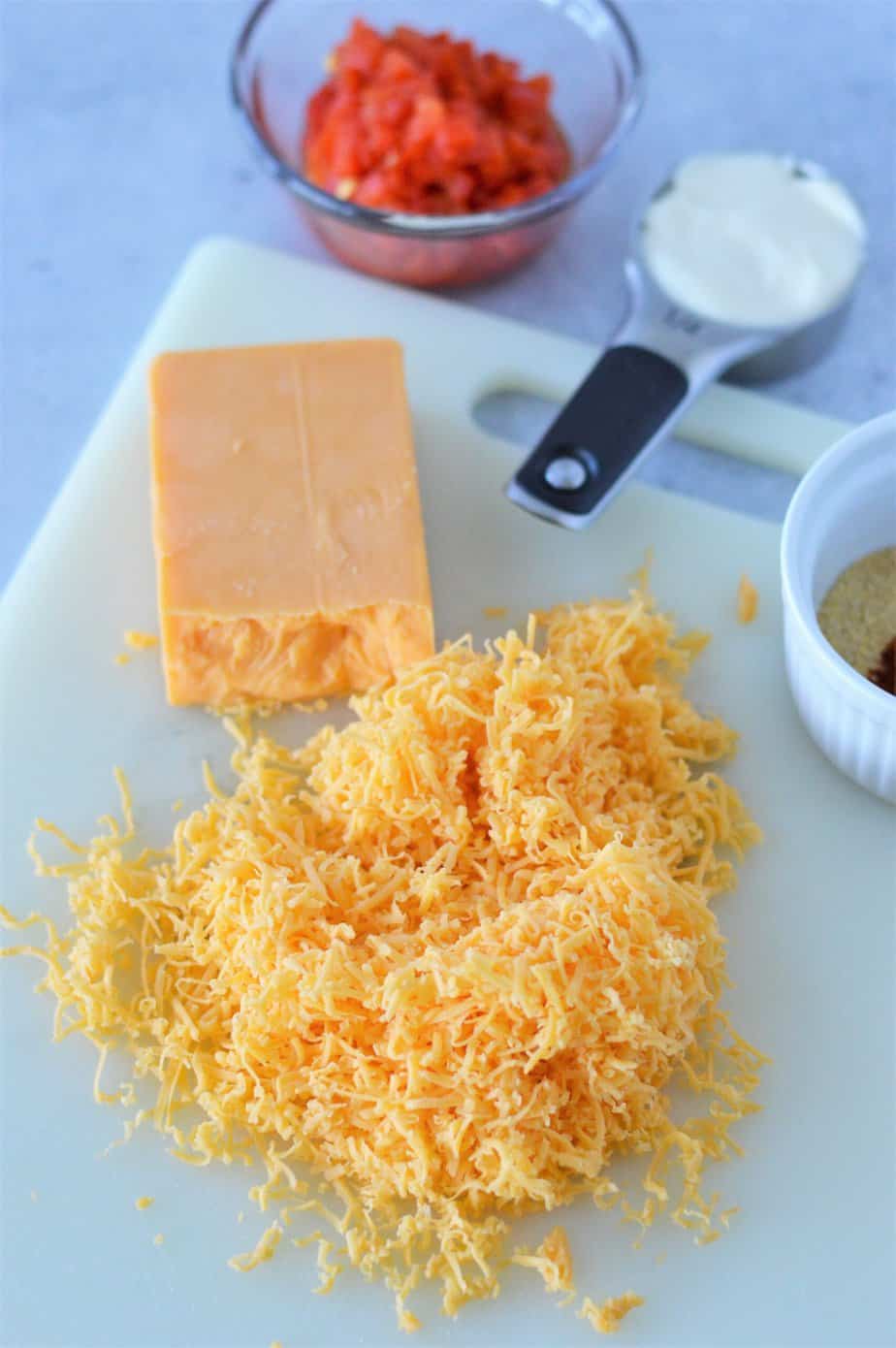 shredded cheddar cheese on cutting board and other ingredients for pimento cheese