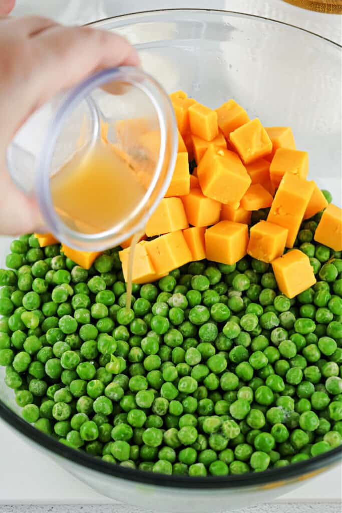 peas in clear glass bowl with cheese, pouring apple cider vinegar over