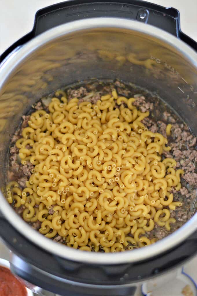 elbow macaroni in instant pot with cooked ground beef, broth and seasoning