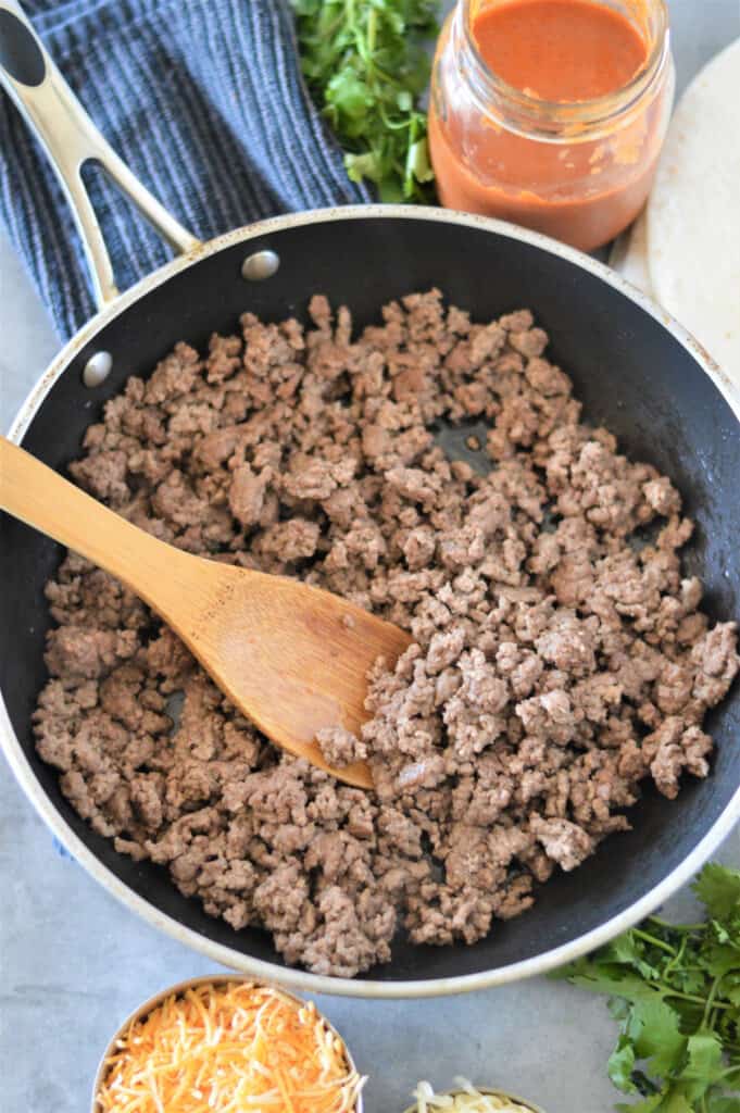 ground beef cooked in skillet with enchilada sauce in jar