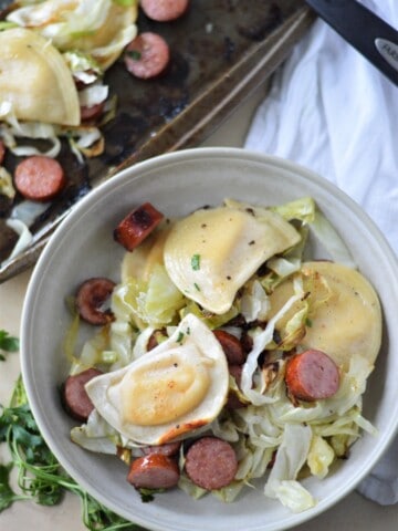 roasted cabbage, smoked sausage and pierogies in a bowl next to sheet pan of food
