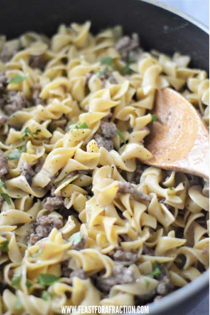 close-up of beef stroganoff garnished with chopped parsley in skillet with wooden spoon