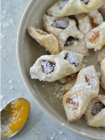 overhead view of Kolaczki cookies on platter with spoon of fruit filling in background