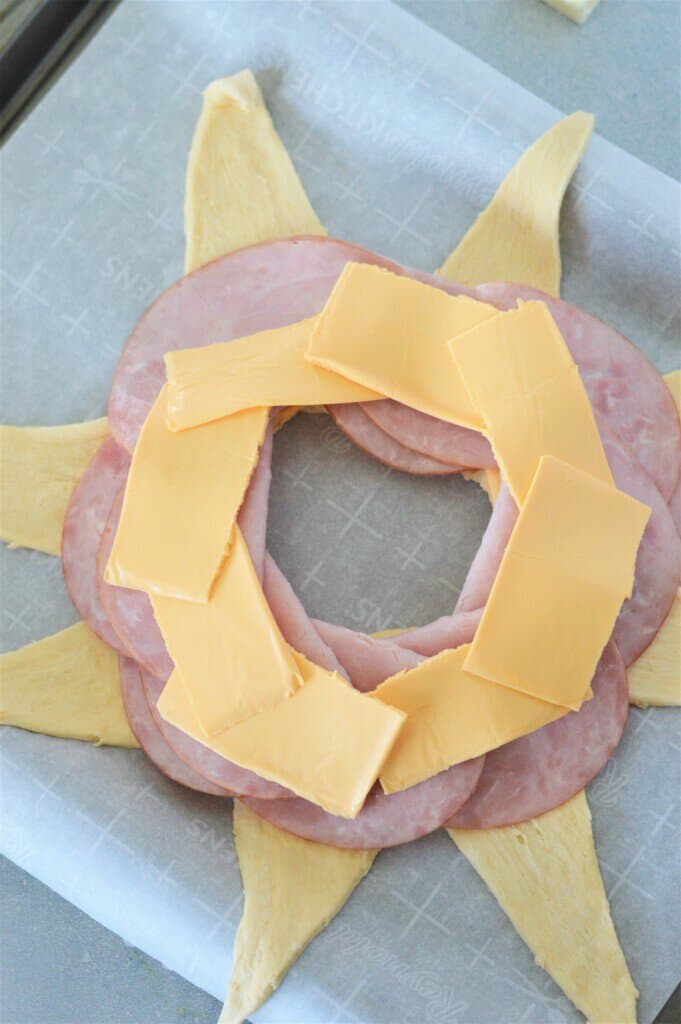 overhead view of crescent roll dough, deli ham, and American cheese layered on a sheet pan